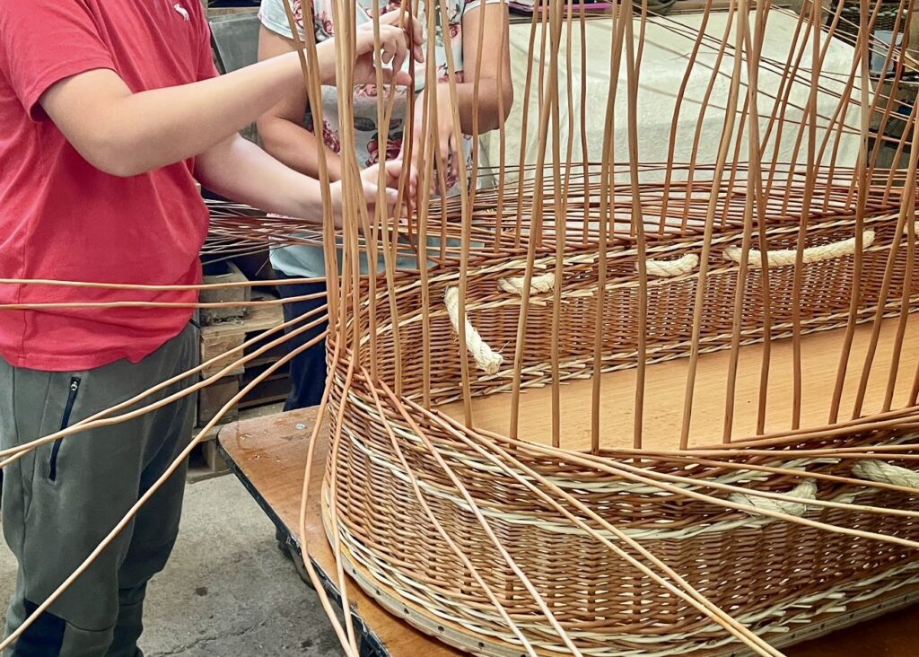 Two pairs of hands helping to weave a coffin