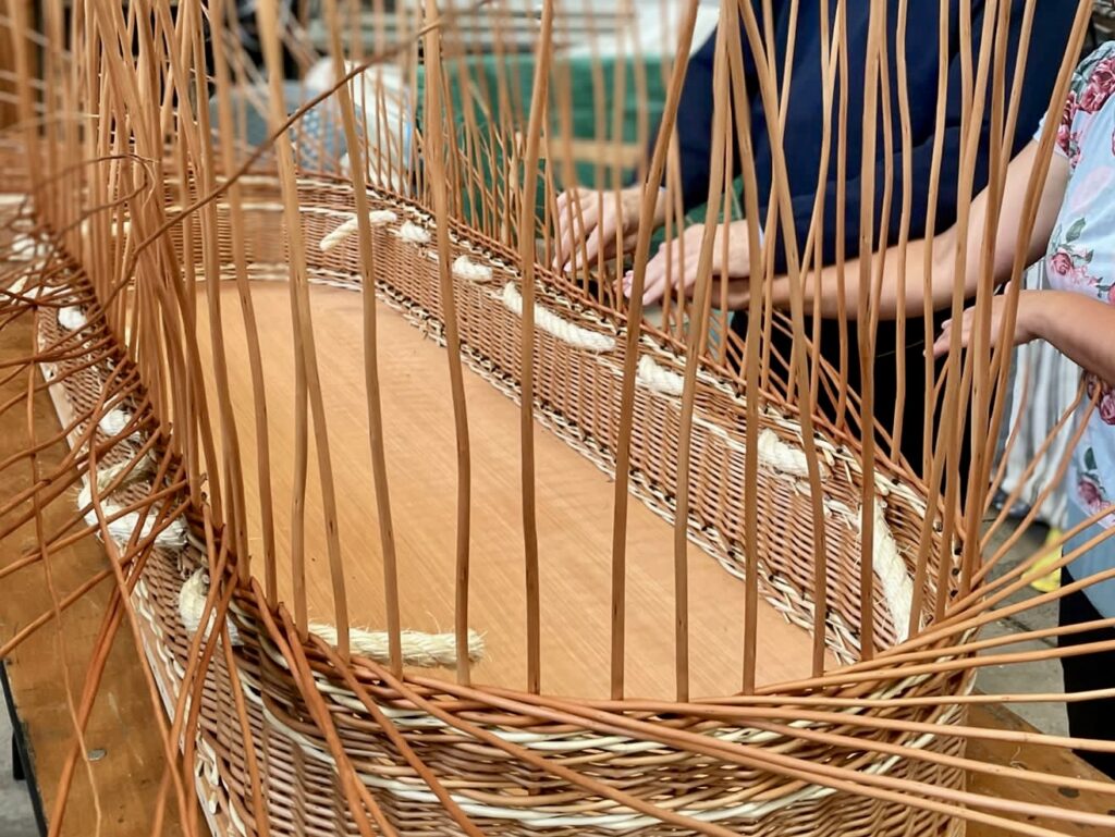 Two pairs of hands weaving the side of a buff willow coffin.