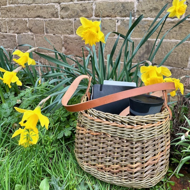 Catalan handbag sat on the grass next to yellow daffodils.
