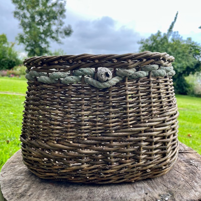 Black maul basket sat on a log in a garden.