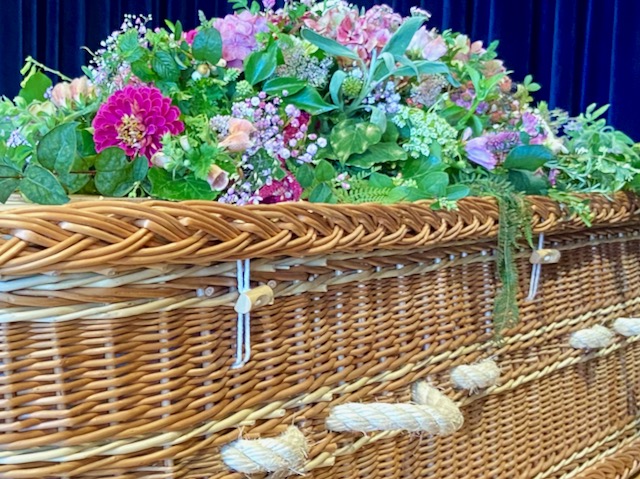 Side profile of buff willow coffin with British flowers displayed on the lid