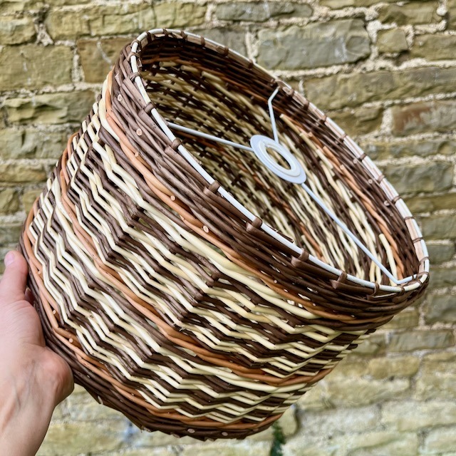 Hand holding buff, buff noir and white willow lampshade against stone wall.