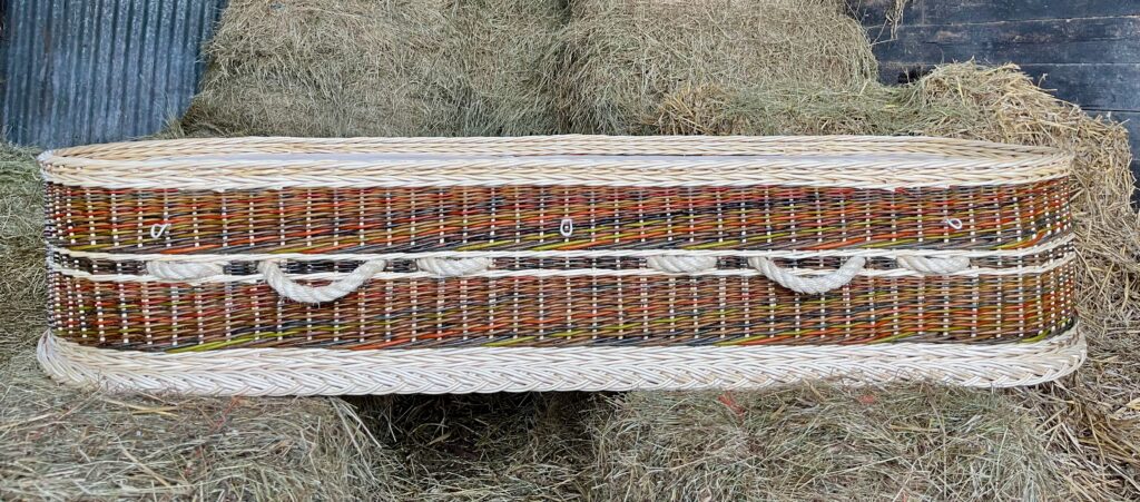 Side view of colourful willow coffin with white plaits on our hay bales