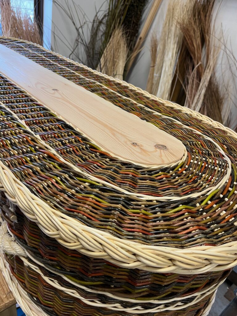 Rounded end of a colourful willow coffin with white plait detail