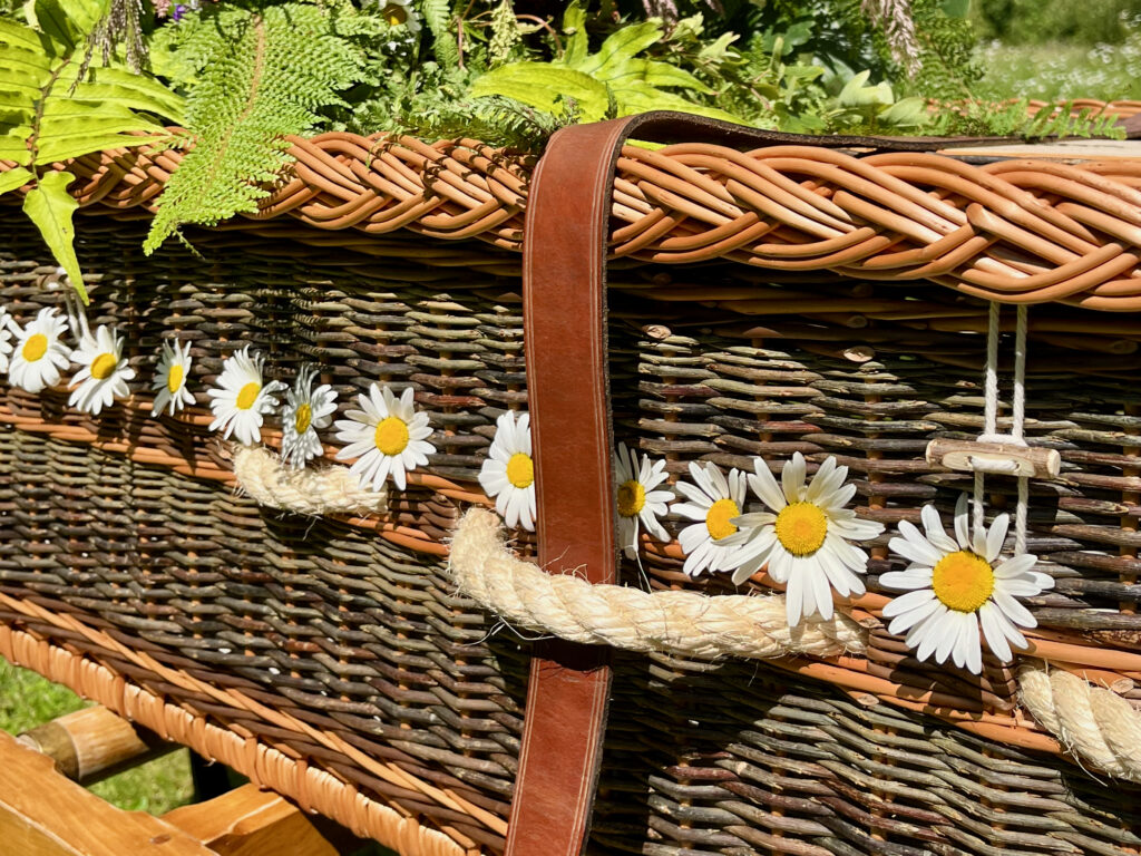 Ox-Eye Daisies woven into the side of a willow coffin with ferns displayed on the top. 