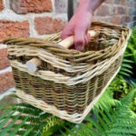 Hand holding a willow handled square basket in front of red brick wall