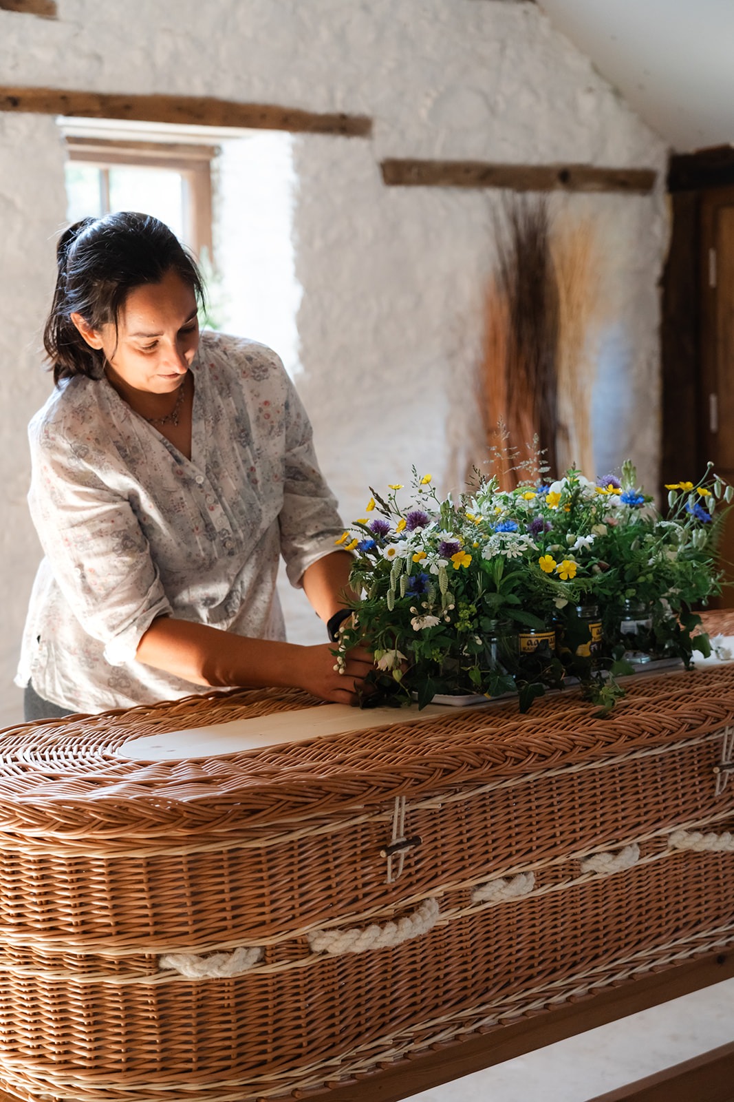 Steph stood arranging flowers that are on top of a coffin in her workshop