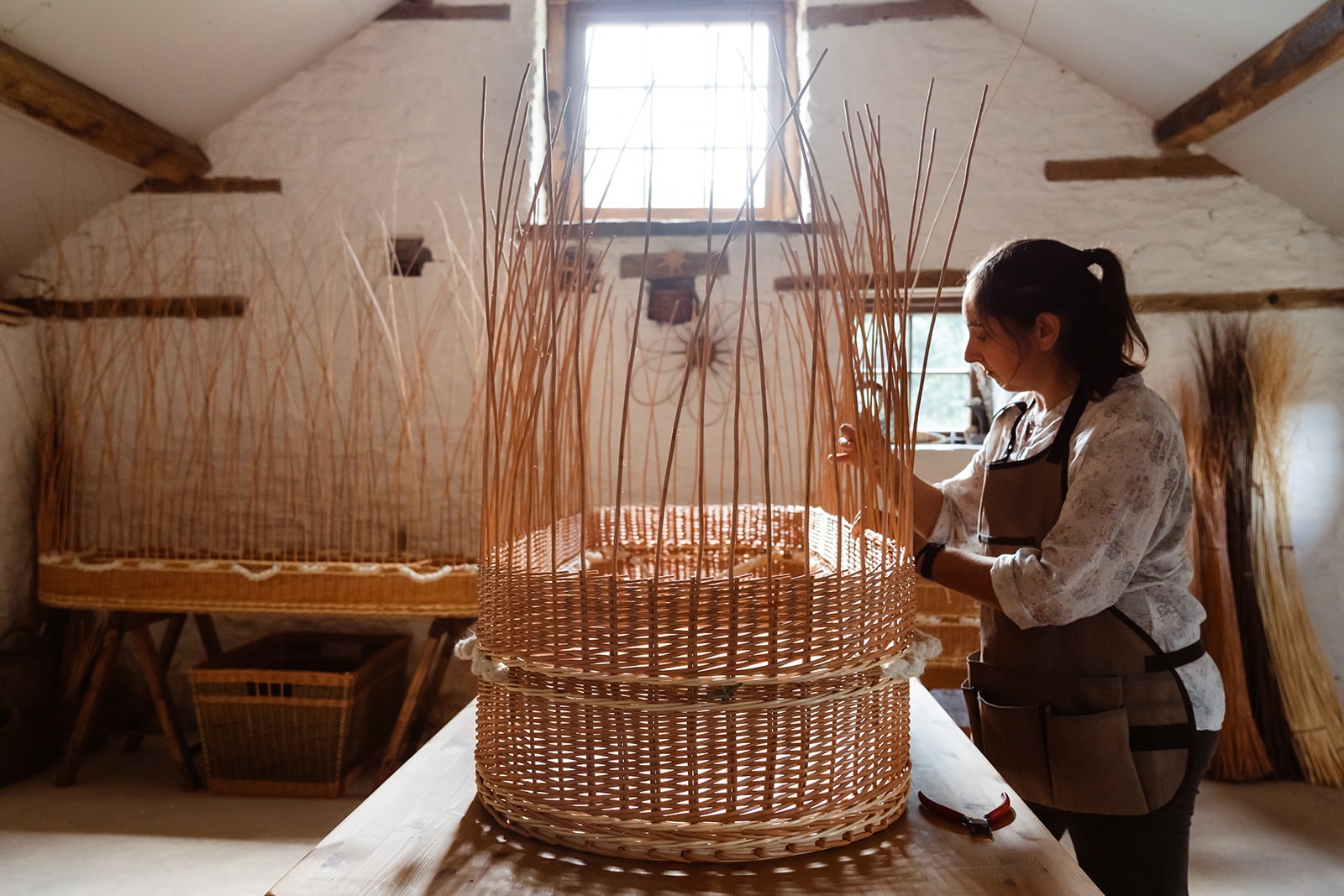 Steph weaving part of a willow coffin in an old stone workshop in morning light