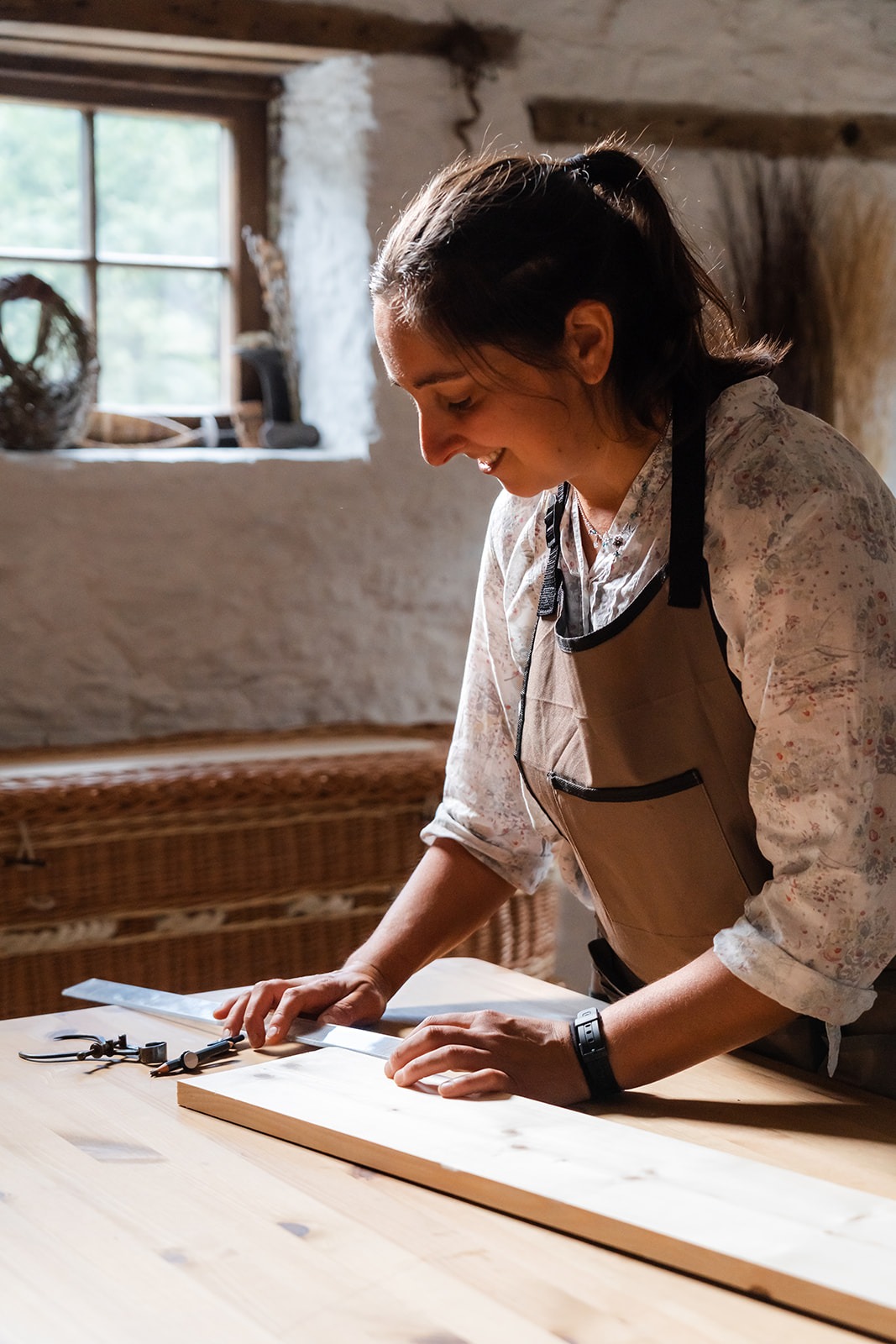 Steph smiling whilst marking up a piece of wood in her workshop for a coffin lid